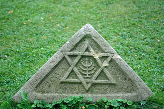 Bild: Stein auf einem Friedhof mit religiösen Symbolen. Hier: Stern und siebenarmiger Leuchter für das Judentum