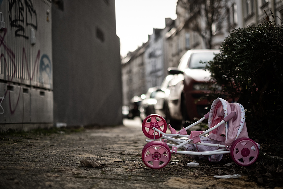 Bild: Weggeworfener alter Spiel-Kinderwagen auf einem Bürgersteig