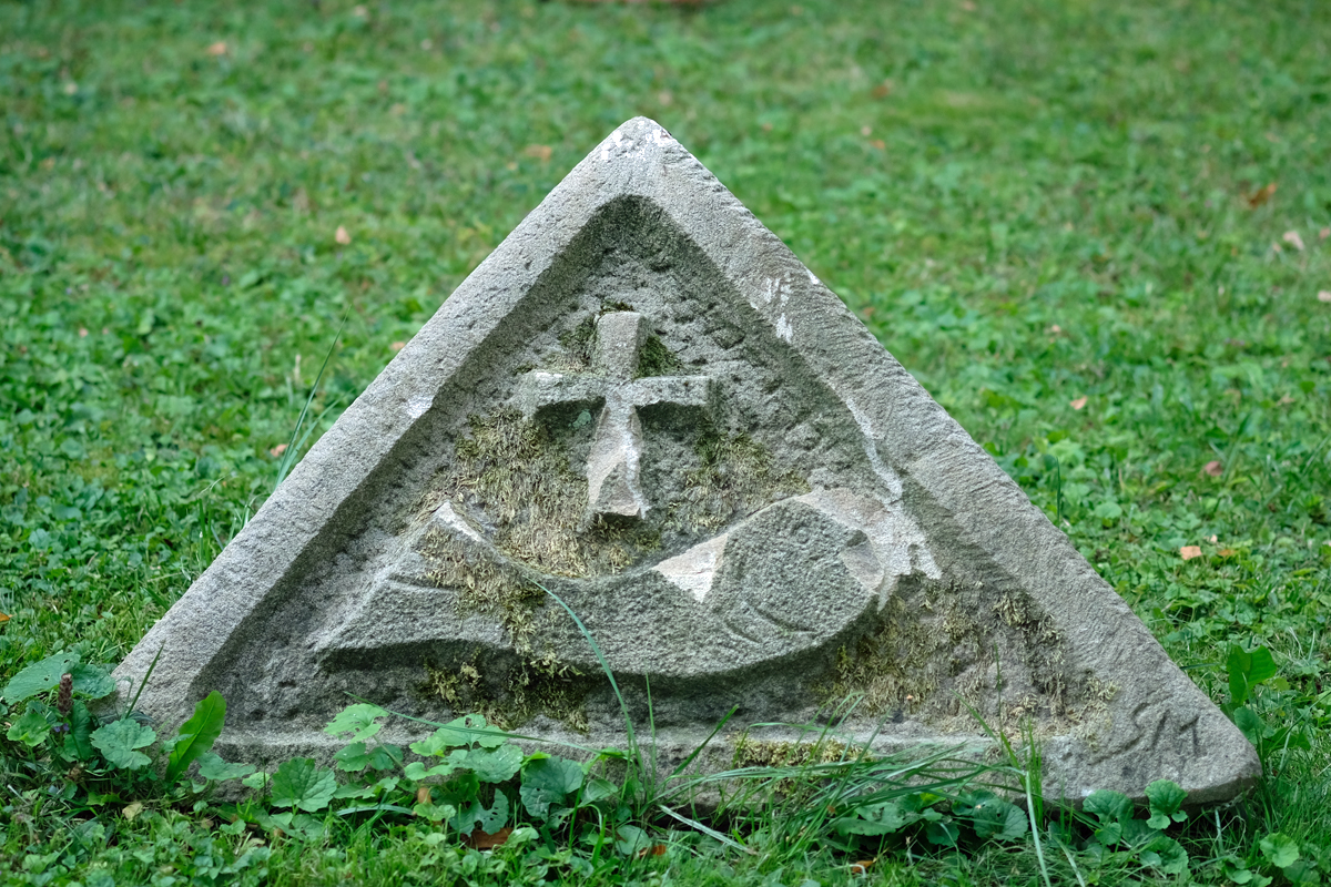 Bild: Stein auf einem Friedhof mit religiösen Symbolen. Hier: Kreuz und Fisch für das Christentum